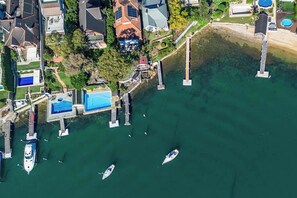 Aerial view of a marina with various boats docked, located adjacent to waterfront properties and lush green lawns.