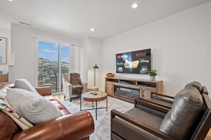 The living room has plush seating, an expansive smart TV, and sliding patio doors that frame the breathtaking mountain vistas.