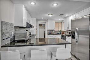 Sleek and functional kitchen featuring granite countertops, stainless steel appliances, ample cabinet space, modern backsplash, and a cozy breakfast bar with seating for two.