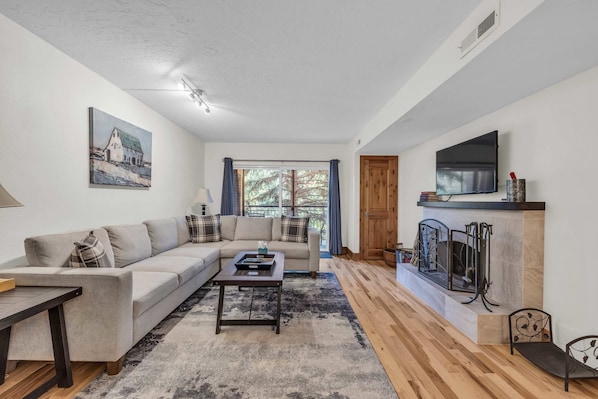 Living Room: L-shaped couch, a wood-burning fireplace, 55” Smart TV w/cable, access to the balcony 
