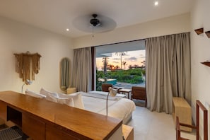 Enjoy a restful night in this elegant bedroom with floor-to-ceiling curtains, a comfortable king-sized bed, and direct access to a private terrace overlooking the sunset.
