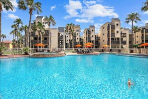 Enjoy a refreshing dip in the expansive outdoor pool surrounded by palm trees and sun loungers, ideal for relaxation under the sun.