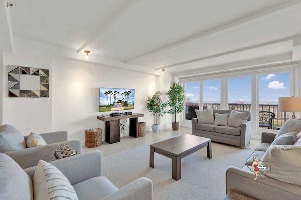 Bright, open living area with comfortable seating, a flat-screen TV, and large windows showcasing scenic surroundings.