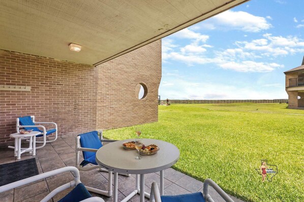 Covered patio with outdoor seating, overlooking a lush green lawn and an expansive view of the horizon.