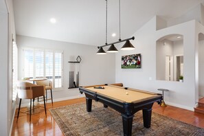 Game room with smart TV, pool table, bar table for two, and lounge chair. (1st Floor)