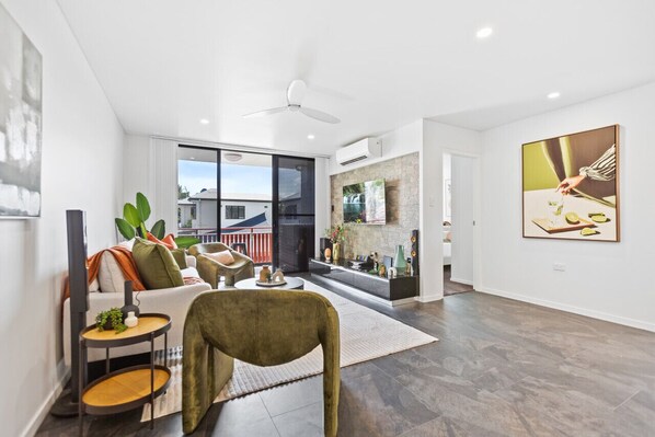 A cozy lounge room filled with natural light, featuring plush seating and stylish decor. Glass doors open to a charming balcony, perfect for enjoying a morning coffee or evening sunset. Ideal for relaxation and indoor-outdoor living