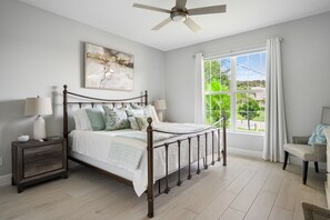 Second bedroom has a king bed with an array of pillows and plush bedding. A ceiling fan and bedside lamp provide warm illumination and great air flow.