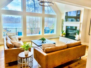 Bright living room with leather sofas, a fireplace, and large windows offering stunning lake views