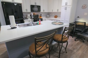 Dedicated workspace with desk, chair, and lamp between kitchen and dining area.
