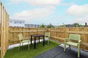 Private outdoor patio featuring a cozy seating area with a black table and vibrant green chairs. Surrounded by a wooden fence for added privacy, the space includes artificial grass and clean tiles, creating a relaxing environment perfect for enjoying fresh air and casual conversations.