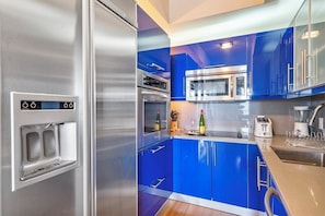 Modern kitchen with Italian blue cabinets, stainless steel refrigerator, microwave, oven, and countertop appliances such as a blender and toaster.