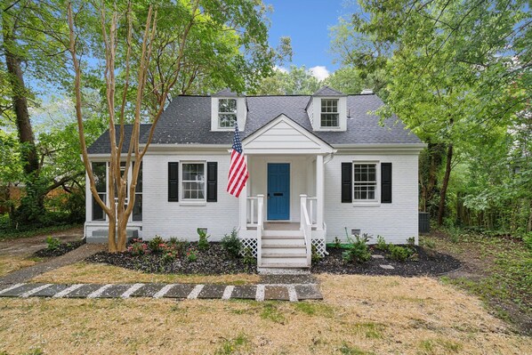 Charming white brick house with a dark roof, blue door, and cute Screened porch