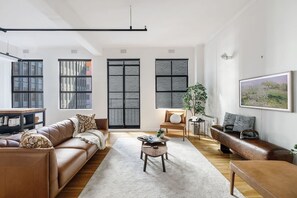 The open-plan living area has a loft-like aesthetic with oversized windows and beam lighting.
