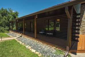Discover the inviting porch of Valley View Getaway, where comfort meets rustic charm. This spacious area features comfortable seating, perfect for enjoying the fresh air while taking in the serene surroundings. The home's log exterior and natural stone accents enhance the cozy vibe, making it an ideal spot for relaxation. The beautifully landscaped path leads you to this welcom...