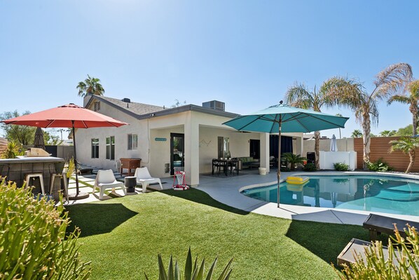 Sparkling heated optional pool, sun loungers, custom-built BBQ area, mobile cooler, cornhole, floating basketball hoop, outdoor dining table, patio furniture, and ample lounge areas.