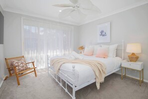 Relax in the serene main bedroom featuring a comfortable queen bed, ceiling fan and a mounted TV.