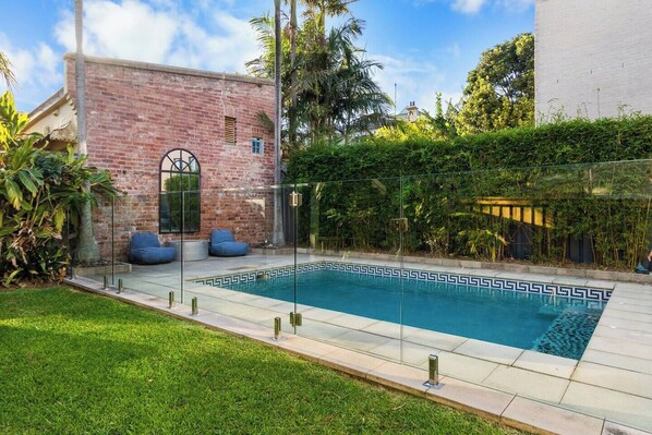 Relax by the private pool, framed by lush greenery and a charming brick wall backdrop, perfect for enjoying sunny afternoons.
