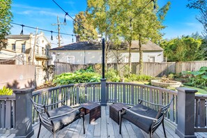 Cozy outdoor seating area overlooking a lush garden with a serene fountain, surrounded by string lights for evening charm.