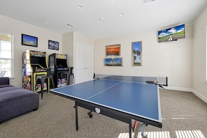 This entertainment space boasts a ping pong table, two classic arcade game machines, and wall-mounted decor. It's a fantastic spot for family fun or a friendly competition among guests.