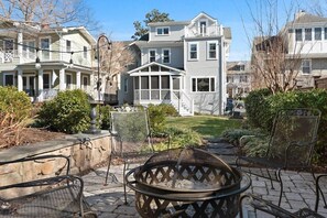 View of the home from the backyard patio with seating around the wood-burning firepit.