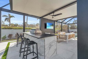 This additional covered area has a ceiling fan, a very large TV, the outdoor kitchen and another seating area 