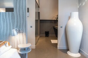 A modern and elegant room featuring sleek decor, soft lighting, and a spacious layout. The minimalist design is complemented by a large statement vase and convenient furnishings, offering both style and comfort.