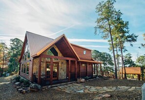 A welcoming cabin exterior with a rustic charm, nestled among tall pines and inviting you to step inside.