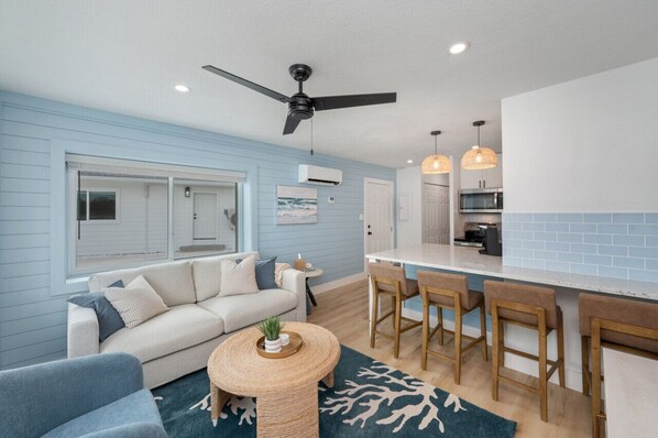 Comfort Open-concept living space with the kitchen just beside the cozy living room, creating a seamless flow for both cooking and relaxation.convenience in this living area, with a ceiling fan, AC, and a peek into the kitchen.
