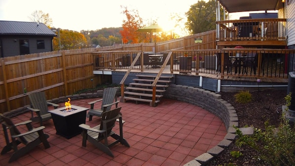 The inviting fire pit patio area is the perfect gathering spot, featuring four comfortable Adirondack chairs for relaxation and conversation. A propane heater ensures warmth and coziness during cooler evenings.