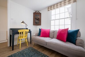 The living room has a large comfy sofa with velvet cushions, a wooden floor and cosy rug. There is also a desk.