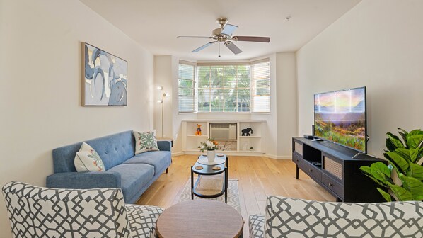 Cozy living room with AC, ceiling fan, flatscreen TV, entertainment center, WiFi, cable, sofa, coffee table, accent chairs, and floor lamp—perfect for relaxing or gathering.
