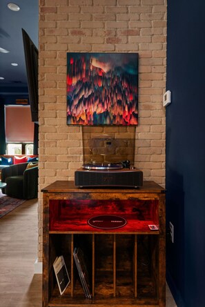 A cozy corner with a vintage record player, set against a brick accent wall, complete with vibrant artwork and a vinyl storage space that adds to the room’s artistic charm.