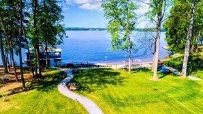 Expansive lakeside property with a sandy beach, lush green lawn, and scenic pathway leading to the water