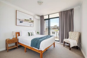 The spacious primary bedroom is appointed with a queen-size bed, side tables and reading lamps, and mirrored built-in robes.