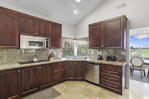 Granite countertops, stainless steel appliances, dark wood cabinetry, and view into dining area
