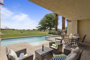 Poolside seating area with lounge chairs, dining table, and golf course view.