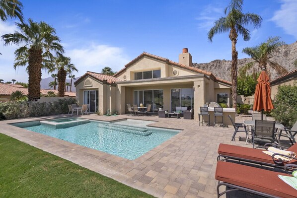 Backyard view: Pool, hot tub, patio seating, and BBQ area surrounded by palm trees