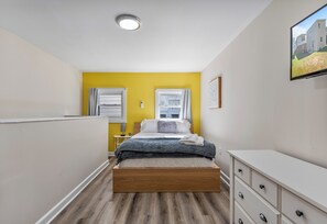 Relax in our airy bedroom with a bright yellow accent wall and serene vibes.