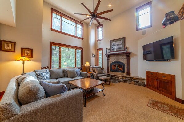Open living room with large sectional sofa, wood burning fireplace & TV.