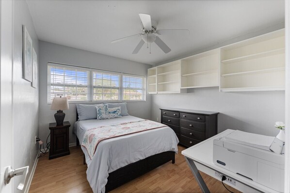 Relax in this bright queen bedroom featuring cozy bedding, ample natural light, and built-in shelving for convenience. A spacious dresser and a sleek desk offer functionality and style, making this room perfect for both rest and productivity.