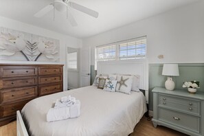 Experience ultimate comfort in this elegant queen bedroom featuring coastal-inspired decor, a luxurious bed, and fresh linens. A spacious dresser and bedside table add convenience, while natural light creates a bright, inviting atmosphere."