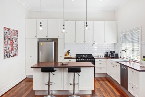 Discover a contemporary kitchen featuring polish white cabinets, a warm wooden countertop, and a spacious large fridge. The open layout seamlessly connects to the dining area, creating a bright and inviting space for cooking and entertaining.