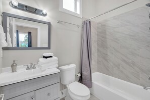 Enjoy a refreshing start to your day in this sleek, fully-equipped bathroom featuring a spacious vanity, ample towels, and a relaxing shower with marble-inspired tile. Perfect for unwinding after exploring the city!