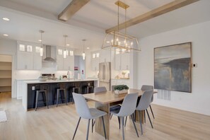 Gather around the elegant dining table for a meal or enjoy a snack at the breakfast bar in this open-concept kitchen, illuminated by natural light and modern pendant lighting