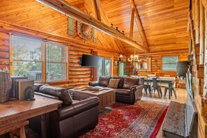 - Relax in the heart of the cabin with plush leather seating and log cabin charm
- Vaulted ceilings, exposed beams, and warm wood walls create a true lodge feel
- Perfect for board games, fireside chats, or dinners at the long farmhouse table