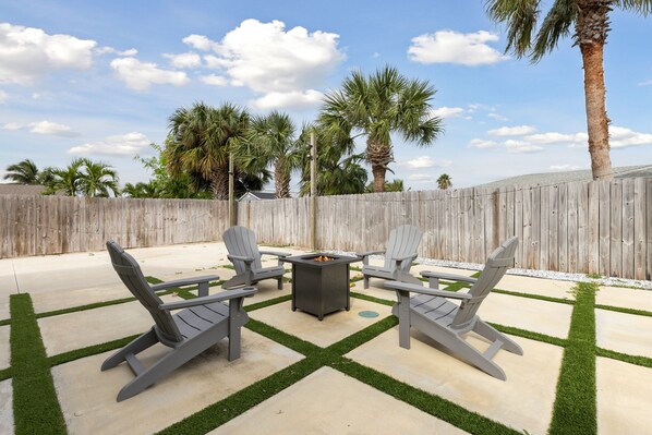 Firepit seating surrounded by palms for cozy, sky-filled evenings.