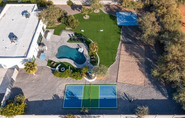 Giant Backyard featuring a pool, mini golf, cornhole, basketball court, sand volleyball, pickleball court, ping pong table, sun loungers, fire pit, grill, and dining table with seating for 10 guests.