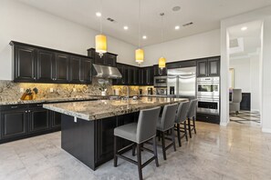 Spacious gourmet kitchen with sleek black cabinetry, a large granite island, and modern appliances.