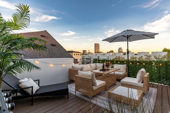 A rooftop patio with comfortable seating area, city view and ambient lighting