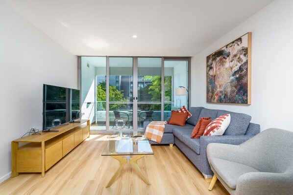 A modern living and dining space with clean, stylish furniture. The dining area features a sleek table and chairs, while the living area includes a comfortable lounge and a smart TV.